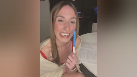 Media: Video of a smiling Caucasian woman with straight brown hair, wearing a beige cardigan, holding a blue toothbrush, studying a book in a dimly lit room.