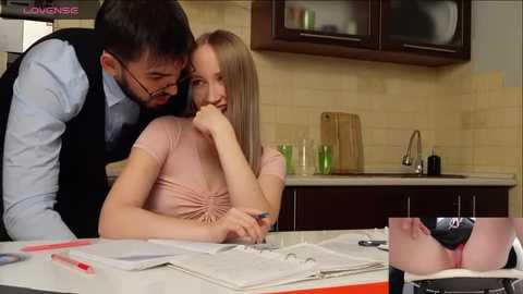 Media: A video depicts a blonde woman in a pink top, leaning on a desk, with a man kissing her neck in a modern kitchen.