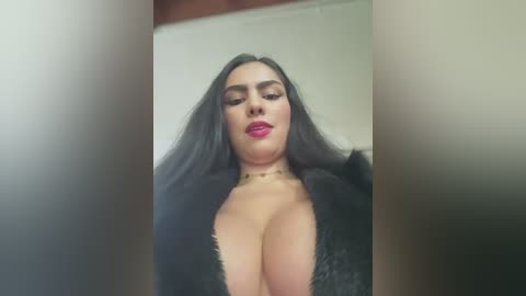 Media: Video of a woman with long, dark hair, wearing a plunging black fur coat, revealing ample cleavage. She has fair skin and wears bold red lipstick. The background is blurred, focusing on her face.