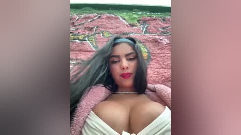 Media: Video of a Latina woman with long dark hair, wearing a pink fuzzy cardigan, exposing her large breasts, in a pink and green landscape background.