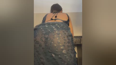 Media: Video of a woman with medium-length dark hair, wearing a black bra and see-through patterned skirt, leaning over a counter.