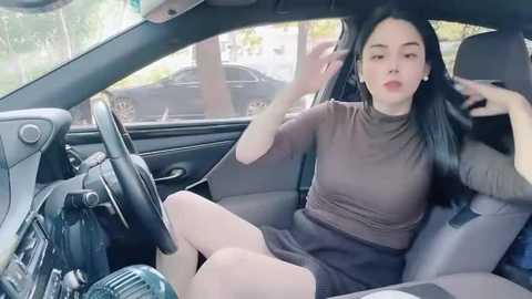 Media: Video of an Asian woman with long black hair, wearing a brown turtleneck and black skirt, adjusting her hair in a car.