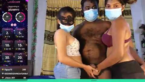 Media: Video of three Black individuals in a dimly-lit room, wearing face masks and revealing attire. One is shirtless, one is in lingerie, and the other is topless. The background includes a TV screen displaying live streaming stats.