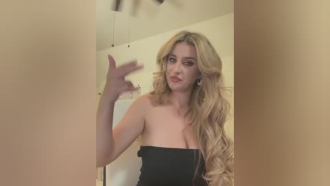 Media: Video of a light-skinned, blonde woman with voluminous curls, wearing a strapless black dress, making a hand gesture in a beige room with exposed electrical wires and a ceiling fan.