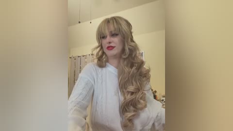 Media: Video of a blonde woman with wavy hair, wearing a white sweater, standing in a beige bathroom with a shower curtain.