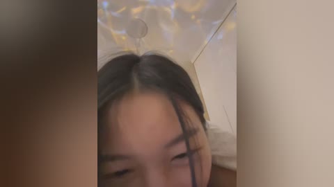 Media: A blurred video of a young Asian woman with long black hair, looking down, partially obscured by a brown blur. The background shows a ceiling with white and gold patterns.