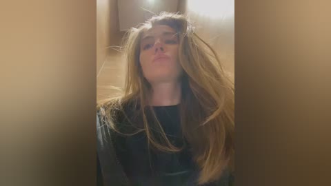 Media: A video of a young woman with long, messy brown hair, wearing a black shirt, standing in a dimly lit hallway. The image is grainy and slightly out of focus.