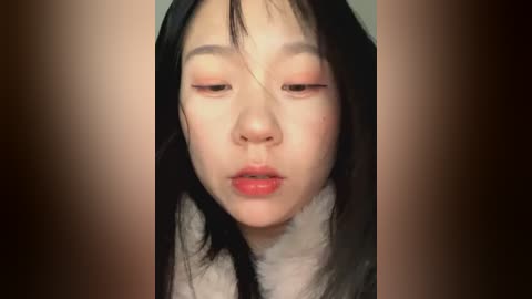 Media: Video of an Asian woman with long black hair, fair skin, and closed eyes, wearing a white fur collar. Background is blurred, focusing on her face.