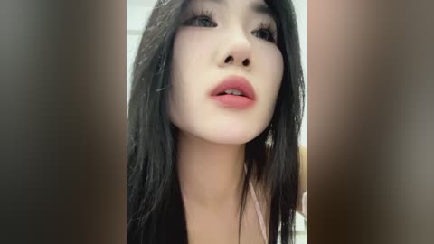 Media: Video of a young Asian woman with long black hair, fair skin, and full lips, wearing pink lipstick and a light top.