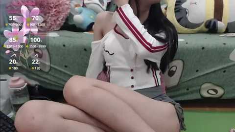 Media: A video of a young woman with long black hair, wearing a white and red striped top and gray skirt, sitting on a green couch with stuffed animals.