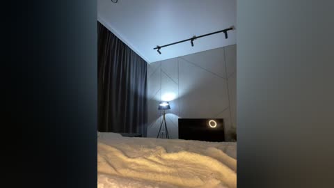 Media: A dimly-lit bedroom video featuring a bed with white sheets, a black stand lamp with a circular light, and dark curtains partially drawn.