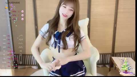 Media: Video of a slender, young Asian woman with long brown hair in a revealing, white and navy blue sailor outfit, smiling playfully. Background features a wooden folding screen and a wooden table with toys.