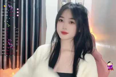 Media: Video of a young East Asian woman with long black hair, fair skin, and light makeup, seated in a modern room with a white robe and black top.