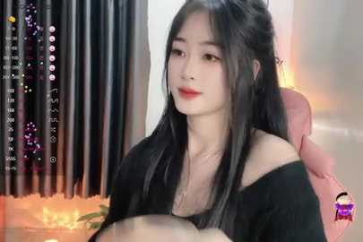 Media: Video of an East Asian woman with long black hair, red lipstick, and a black off-shoulder top, sitting in a plush chair with orange candles behind her.