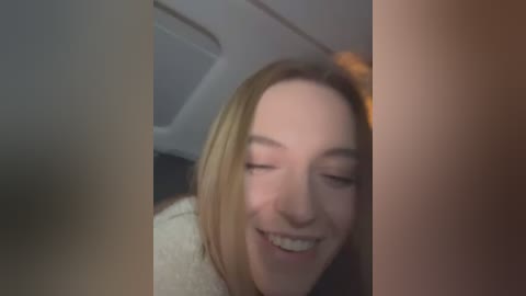 Media: Video of a young woman with light skin and straight blonde hair, smiling and laughing with braces. The background shows a blurry interior of a car.