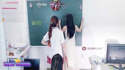 Media: Video of two women in school uniforms, one with a red plaid skirt, writing on a chalkboard, in a classroom setting.