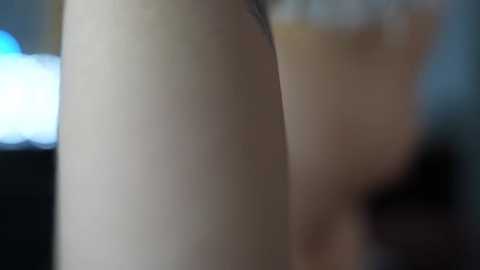 Media: A close-up video of a woman's bare back, showing smooth, pale skin. The background is blurred, featuring indistinct shapes and colors, possibly indoor lighting.