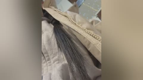 Media: Video of a person lying on a beige blanket, showing a long, straight, black ponytail that falls over the edge of the blanket.