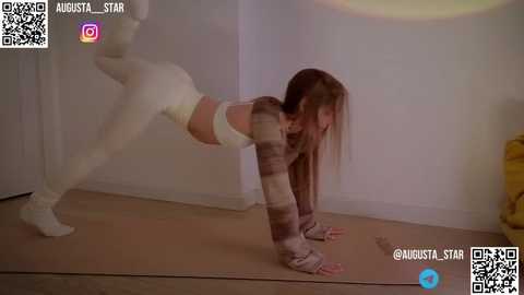 Media: Video of a woman in a striped crop top and leggings doing a plank pose on a mat in a minimalistic room.