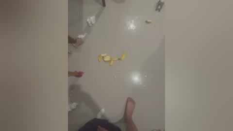 Media: Video of a messy bathroom floor with scattered items including a yellow sponge, a pink bottle, and a white towel. The walls are plain, and the lighting is dim.