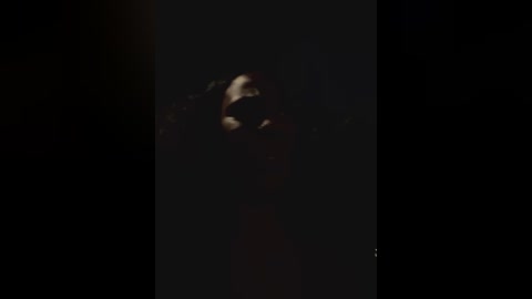 Media: A dimly lit video captures a person with short, dark hair, wearing a dark jacket, partially obscured by shadows, creating an ominous and mysterious atmosphere.