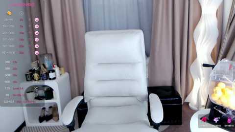 Media: Video of a modern, minimalist living room with a white leather recliner chair facing a large window, beige curtains, and a decorative lamp.