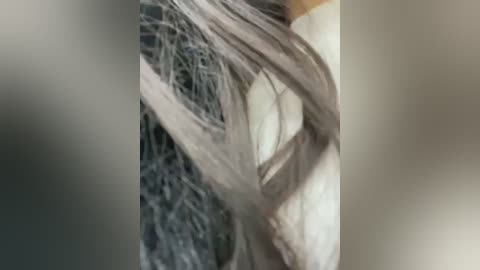 A close-up video of a person's face with long, platinum blonde hair tangled in a web of fine, gray strands. The background is blurred, making the tangled hair the focal point.