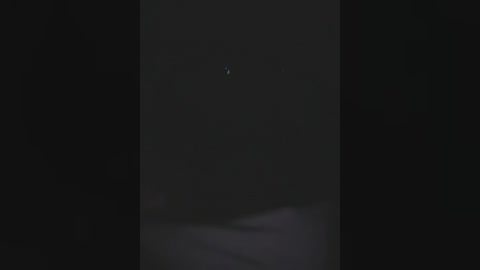 Media: Video of a dimly lit, black and white image with a small, faint crescent moon in the center. The background is blurred and dark, enhancing the moon's visibility. The scene is minimalist and mysterious, evoking a sense of cosmic solitude.