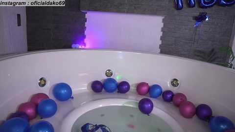 Media: Video of a white bathtub filled with blue and pink balloons, against a gray tiled wall with a purple light in the background.