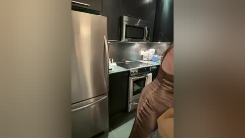 Media: A video of a modern kitchen with stainless steel appliances, black cabinets, and a microwave above the oven. A person, partially visible, wearing a brown apron, stands in the background.