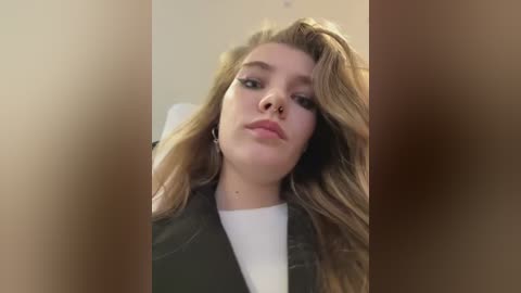 Media: A video of a young woman with long, wavy, blonde hair, wearing a black jacket over a white shirt, taken from a low angle, partially obscured by blurred vertical lines.