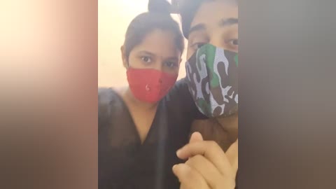 Media: A video shows two South Asian women with medium brown skin, wearing face masks with red and camouflage patterns. They are smiling and holding hands. The background is blurred.