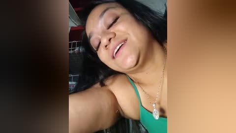 Media: Video of a smiling Latina woman with long black hair, wearing a green tank top, necklace, and visible armpit hair, taken from a close-up angle.