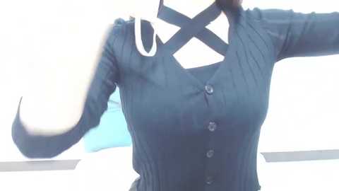 Media: A video of a person wearing a dark blue, button-up shirt with a white, diagonal \"X\" cut-out at the neckline. The background is blurred, showing a white wall with blue accents.