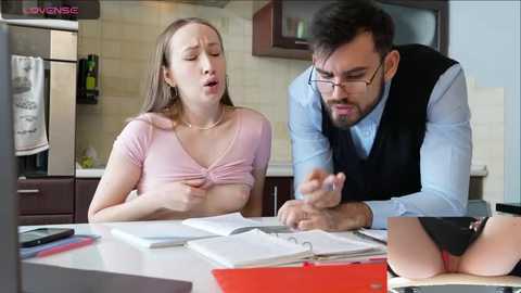 Media: Video of a woman with medium-length brown hair, wearing a pink top, exposed breast, and a man in glasses, dark vest, leaning over her, in a modern kitchen.