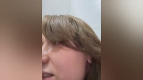 Media: A blurry video of a young woman with fair skin and light brown hair, seen from the side, partially obscured by a blurred brown object.