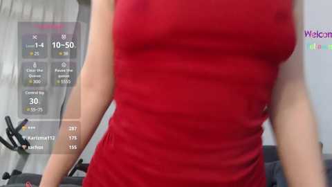 Media: Video of a woman wearing a tight, sleeveless red dress, standing in a modern gym with a virtual reality headset overlay showing fitness stats and progress.