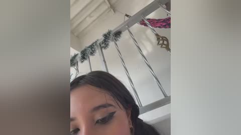 Media: A video of a young woman with long dark hair, wearing heavy black eyeliner, standing indoors near a white window with Christmas garland and a decorative wreath.