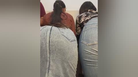 Media: Video of two women with large buttocks, wearing tight, light blue jeans, standing close together in a public bathroom, viewed from behind.