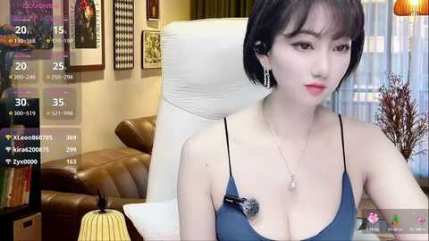 Media: A video of an Asian woman with short black hair and fair skin wearing a blue camisole, posing in a cozy living room with a white chair, framed artwork, and a pumpkin on a table.