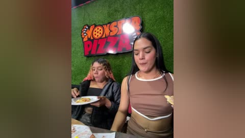 Media: Video of two young women in a restaurant; one with curly hair and a black jacket, the other with straight black hair, wearing a brown top.