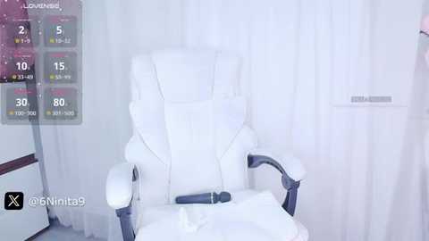 Media: Video of a white leather massage chair with a black remote control, positioned in a minimalist room with white walls and curtains, showing a digital temperature and humidity display on the left.