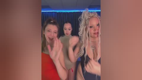 Media: Video of three women in a nightclub, one in a red dress, one nude, and one in a black top, with dark curtains and blue lighting in the background.