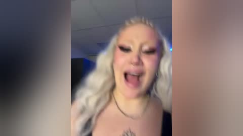 Media: A blurry, grainy video shows a young woman with platinum blonde hair, wearing heavy makeup, and a black top, expressing joy with an open-mouthed smile.