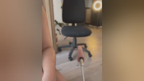 Media: Video of a man's bare buttocks and hand holding a red and white power drill, standing in a modern office with a black office chair and a warm, dimly-lit room.