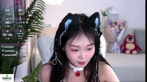 Media: Video of an East Asian woman with long black hair, wearing black cat ears, a white choker, and a red bow, sitting indoors, surrounded by a virtual reality environment.