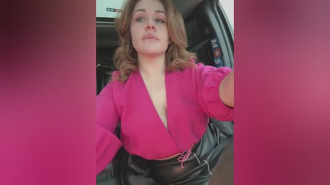 Media: Video of a plus-size woman with light skin and shoulder-length, wavy brown hair, wearing a bright pink blouse and high-waisted black leather pants, seated in a car.