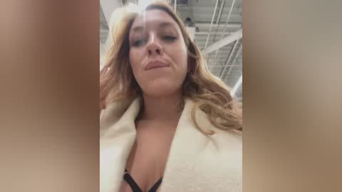 Media: A video captures a close-up of a woman with long, wavy blonde hair, wearing a white robe and black lingerie, indoors with industrial ceiling beams visible.