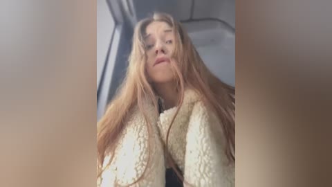 Media: A blurry, low-angle video of a young woman with long, messy blonde hair, wearing a beige knit sweater, looking upward with a neutral expression.