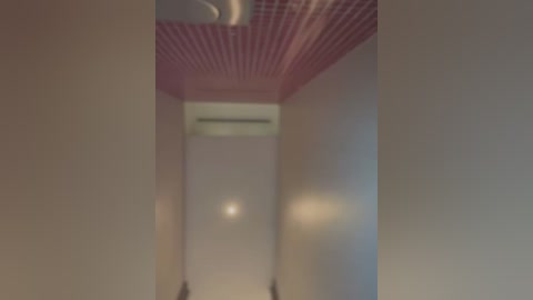 Media: Video of a narrow, beige-painted corridor with a pink, checkered ceiling, an air conditioner unit, and blurred walls.